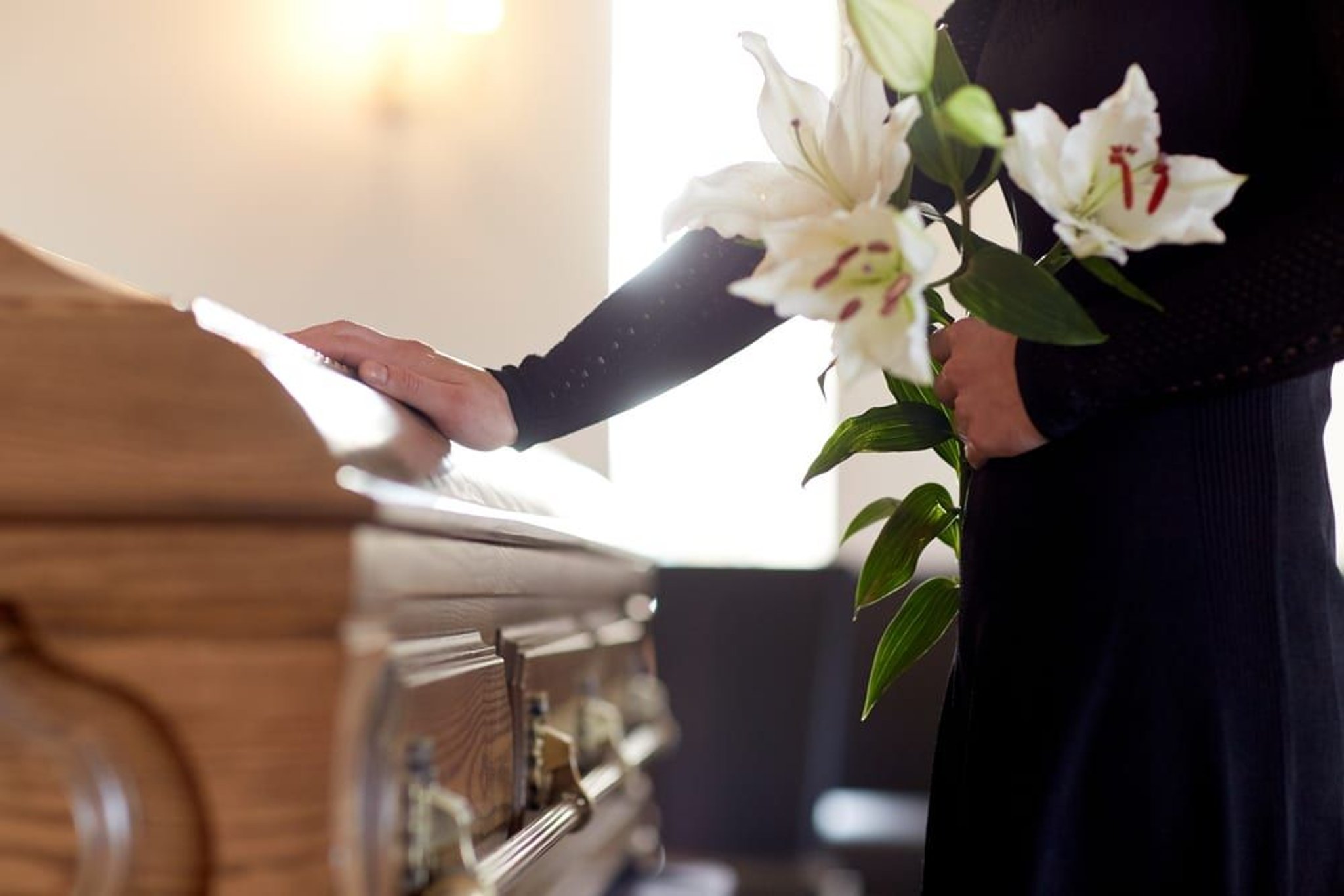 Woman with a flower stands next to a coffin